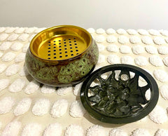 A gold-colored incense burner and holder with a decorative design, displayed on a white textured surface.