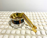 A gold-colored incense burner and holder with a decorative design, displayed on a white textured surface.
