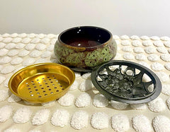 A gold-colored incense burner and holder with a decorative design, displayed on a white textured surface.