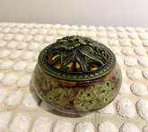A gold-colored incense burner and holder with a decorative design, displayed on a white textured surface.