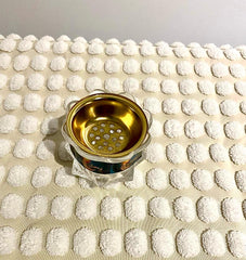A gold-colored incense burner and holder with a decorative design, displayed on a white textured surface.