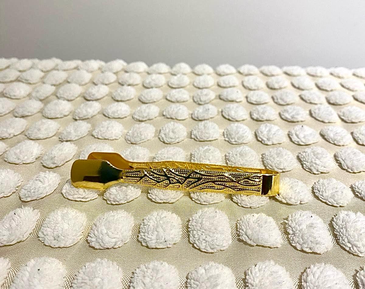 Gold-colored metal tongs with a decorative pattern, placed on a textured white surface.
