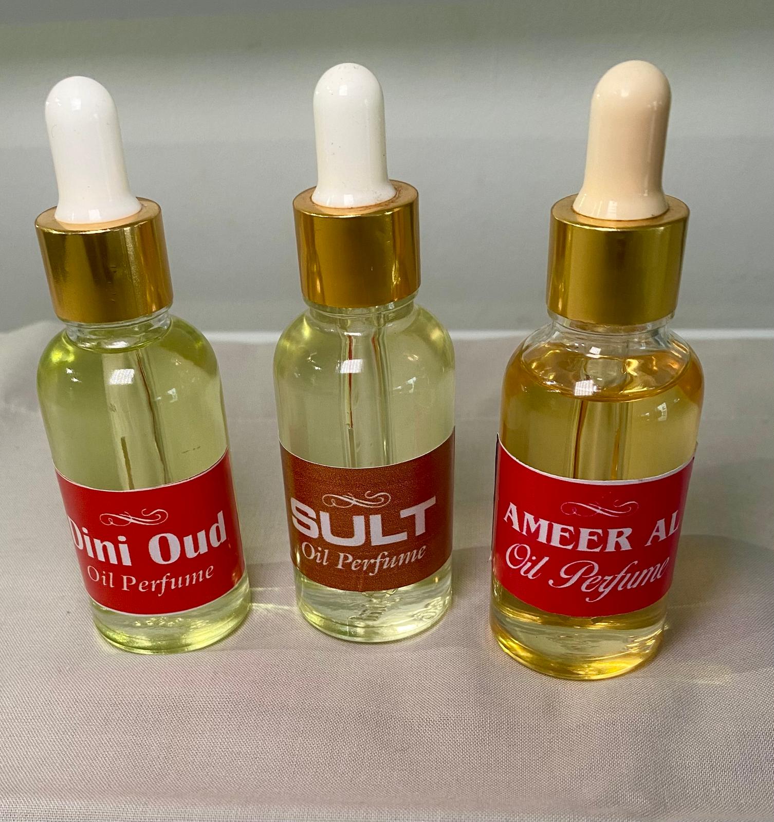 Three glass bottles with white dropper caps, labeled Mini Oud, Oud, and Amer Al Oud Oil Perfume, filled with a yellow liquid.