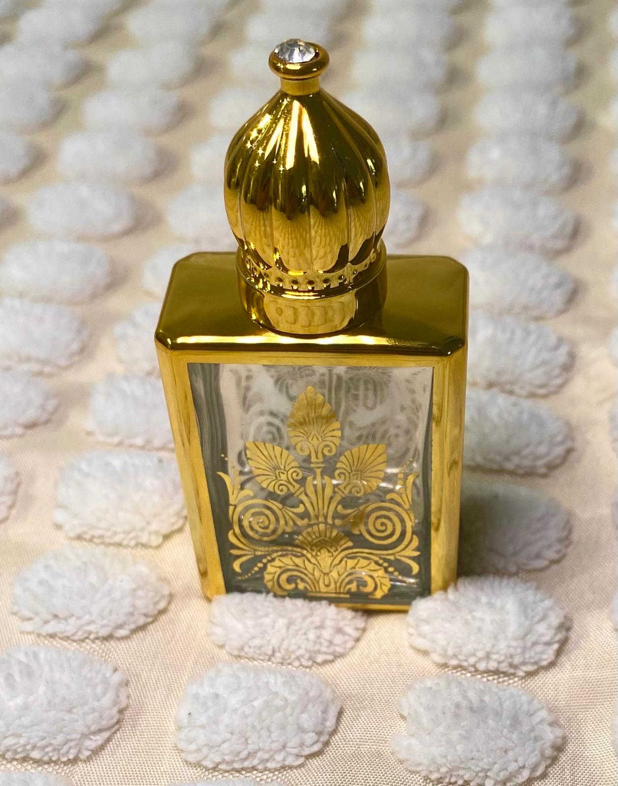 An empty essential oil roller bottle with a gold-colored cap and decorative patterns on the body, displayed on a textured white surface.