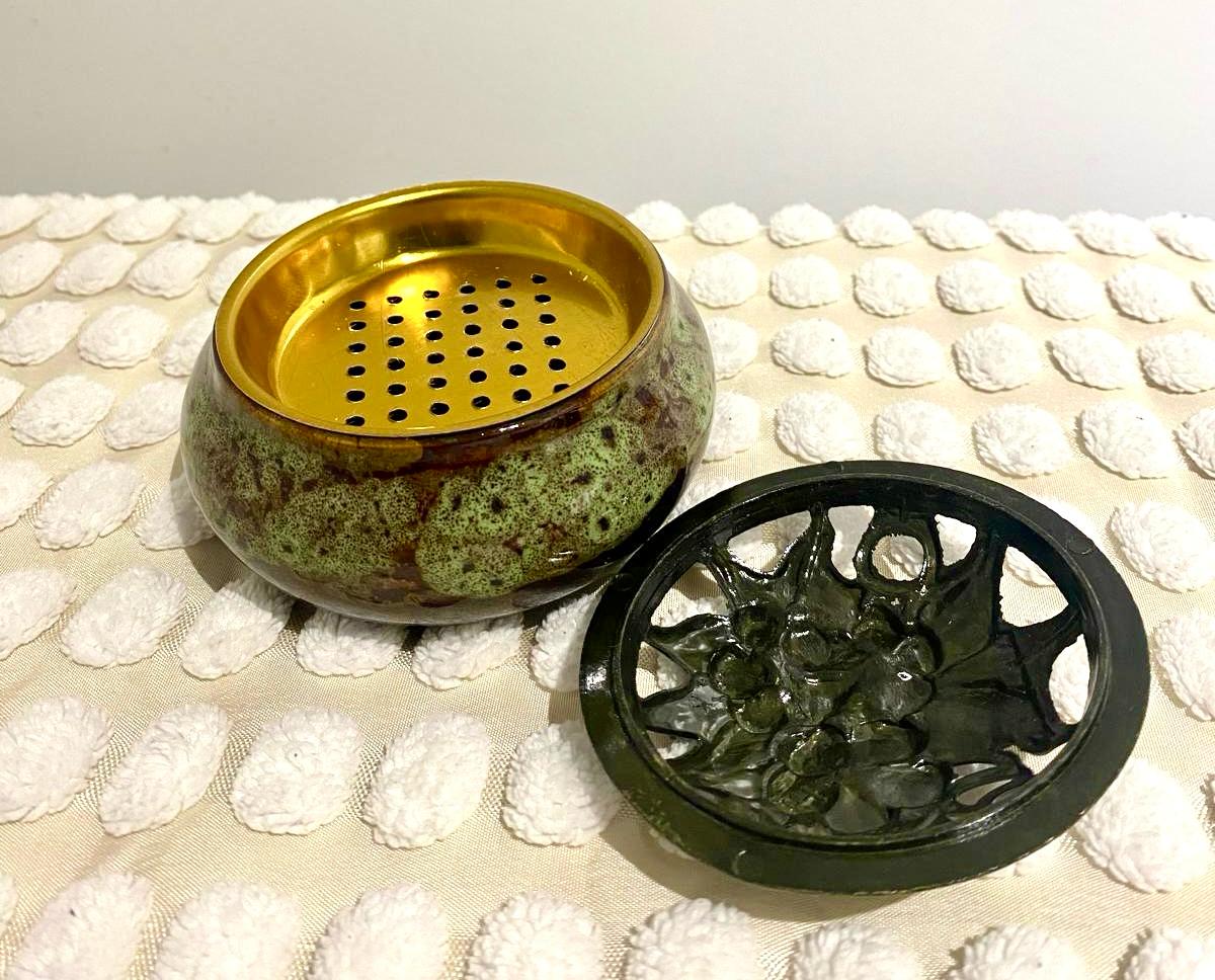 A gold-colored incense burner and holder with a decorative design, displayed on a white textured surface.