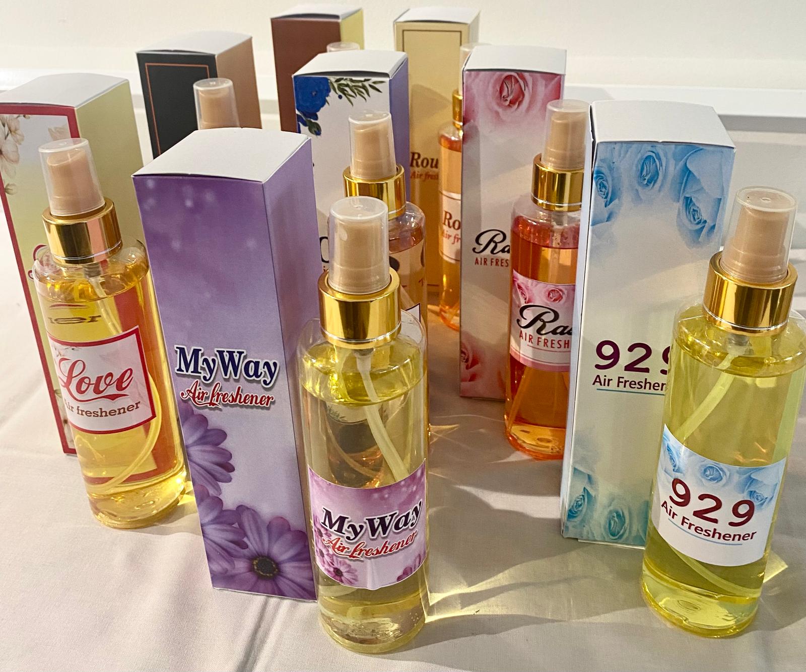 A collection of spray bottles with various home care fragrance labels, displayed on a table. The labels indicate different scent options.