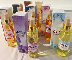 A collection of spray bottles with various home care fragrance labels, displayed on a table. The labels indicate different scent options.