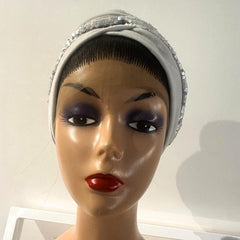 A mannequin head wearing a silver turban with a decorative border.