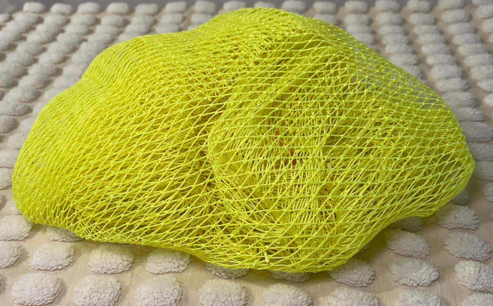 A yellow bath sponge with a net-like texture, placed on a light-colored surface.