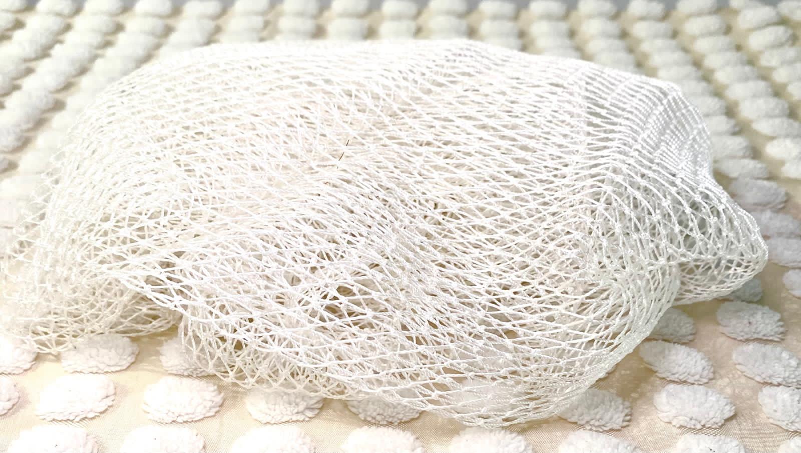 A white bath sponge with a net-like texture, placed on a light-colored surface.