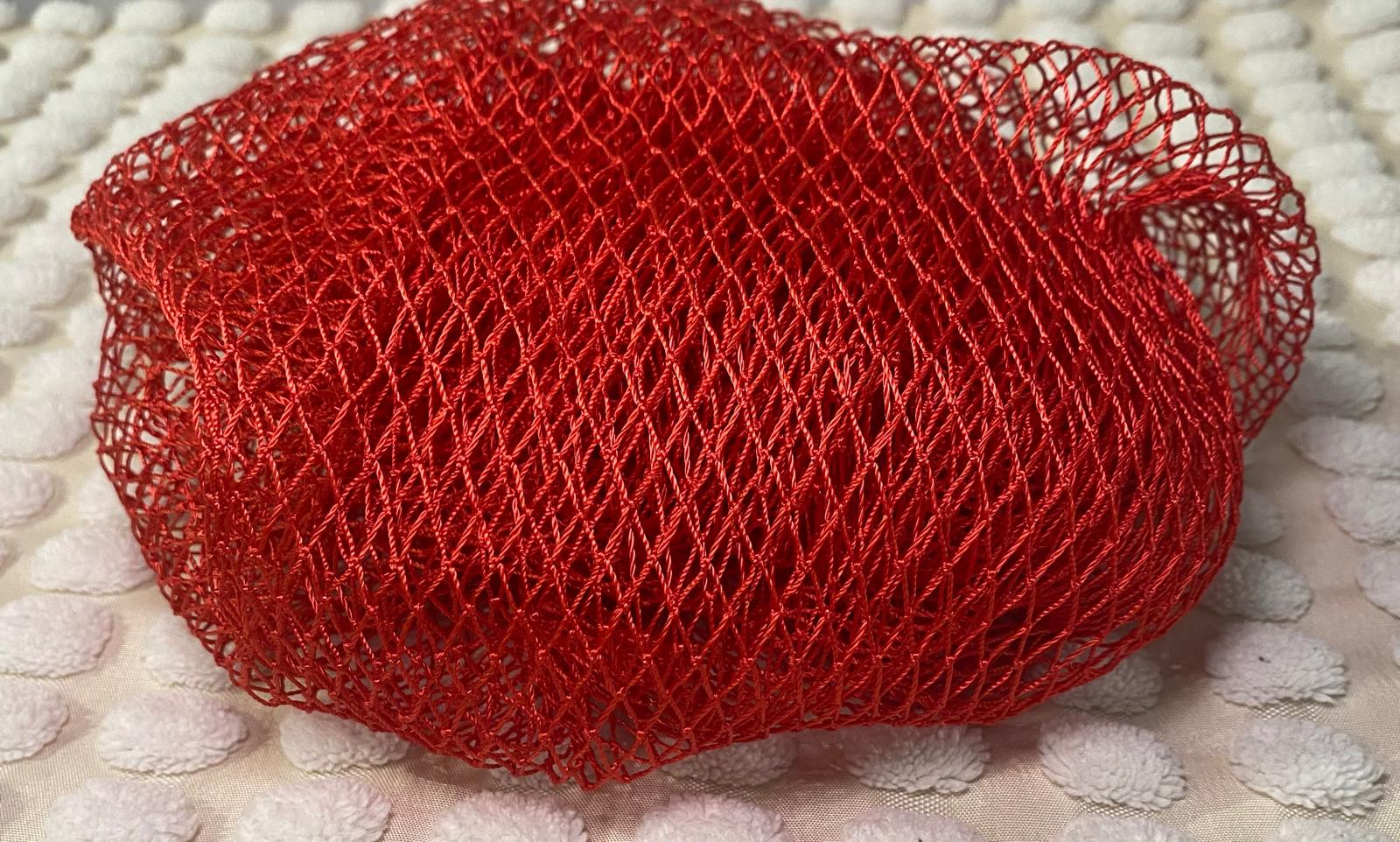 A red bath sponge with a net-like texture, placed on a light-colored surface.