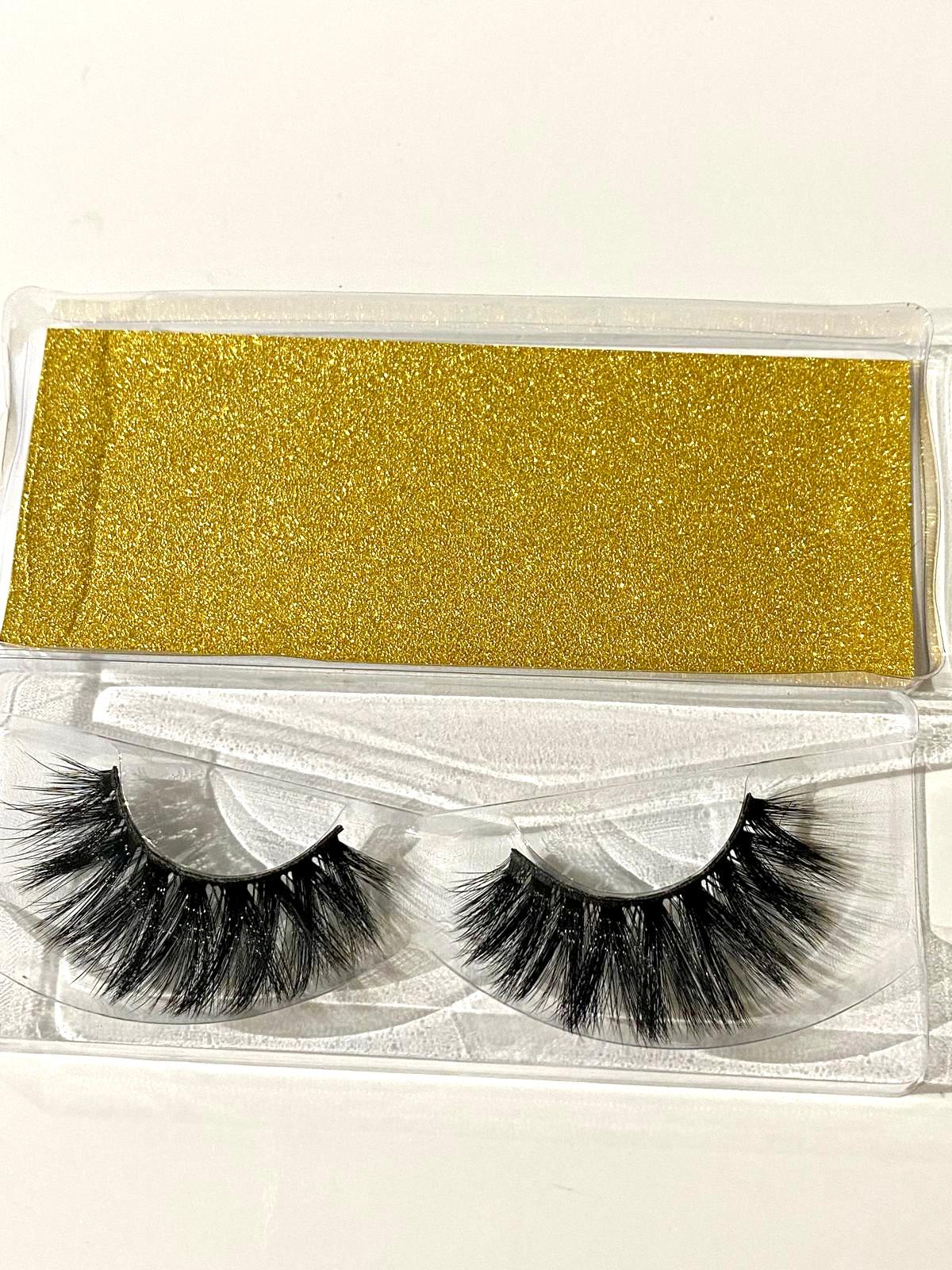 Pair of false eyelashes in a clear packaging with gold color swatch on a white background