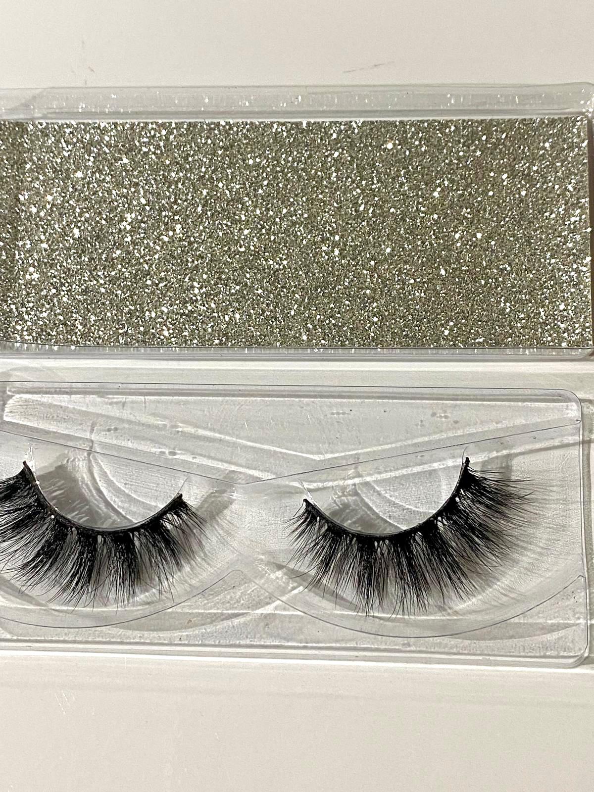 Pair of false eyelashes in a clear packaging case with a glittery silver top.